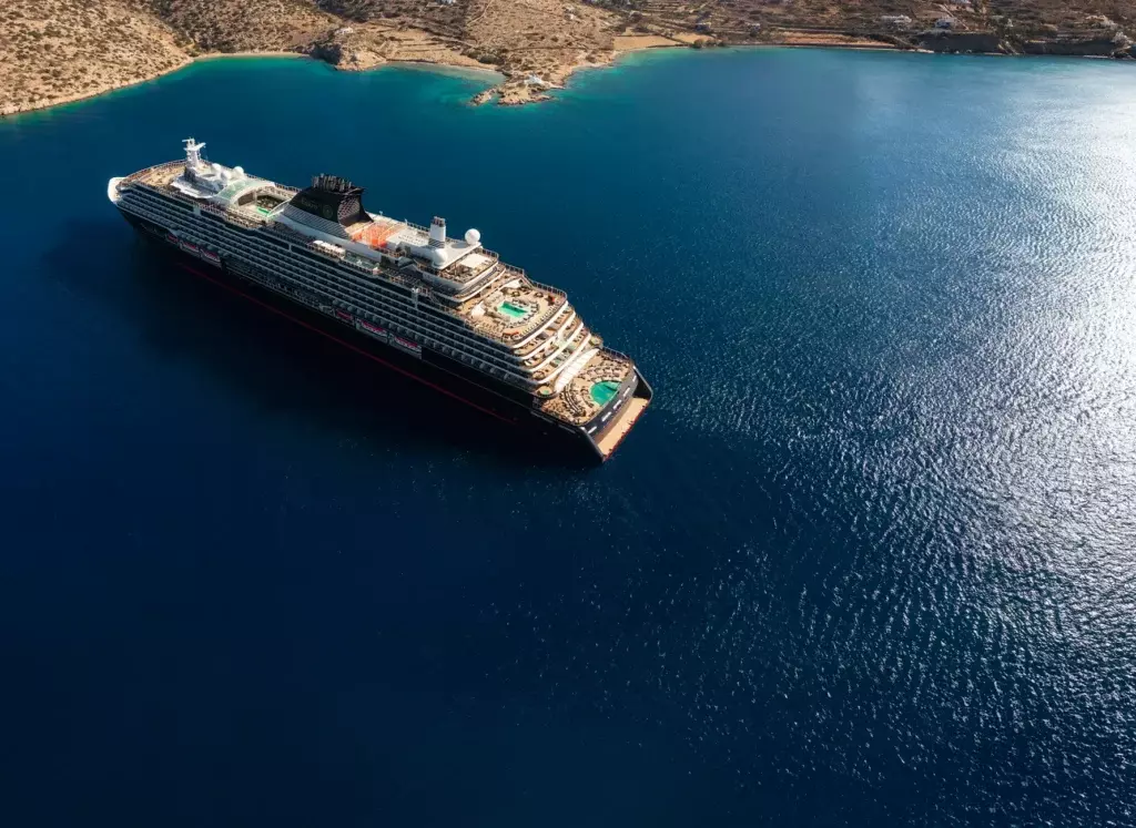 El buque de lujo EXPLORA I navegando cerca de una costa exótica con montañas al fondo