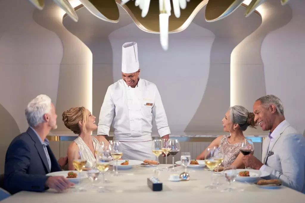 Pasajeros del Oceania Club disfrutando de una cena gourmet exclusiva con atención personalizada del chef ejecutivo en un crucero de lujo.