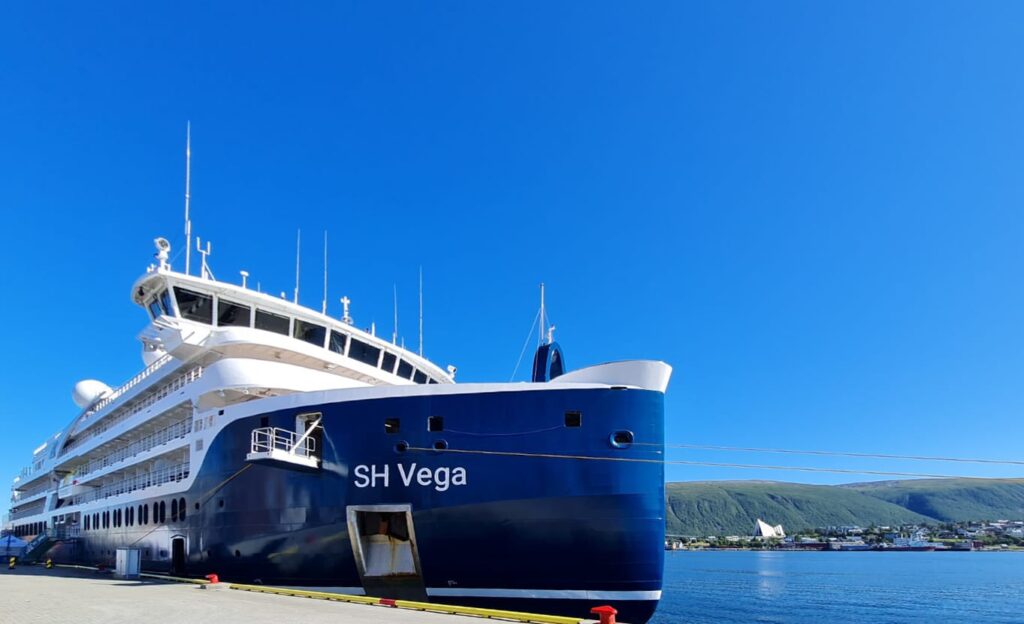 El buque SH Vega de Swan Hellenic atracado en un puerto europeo bajo un cielo despejado mostrando su diseño de proa reforzada para expedición