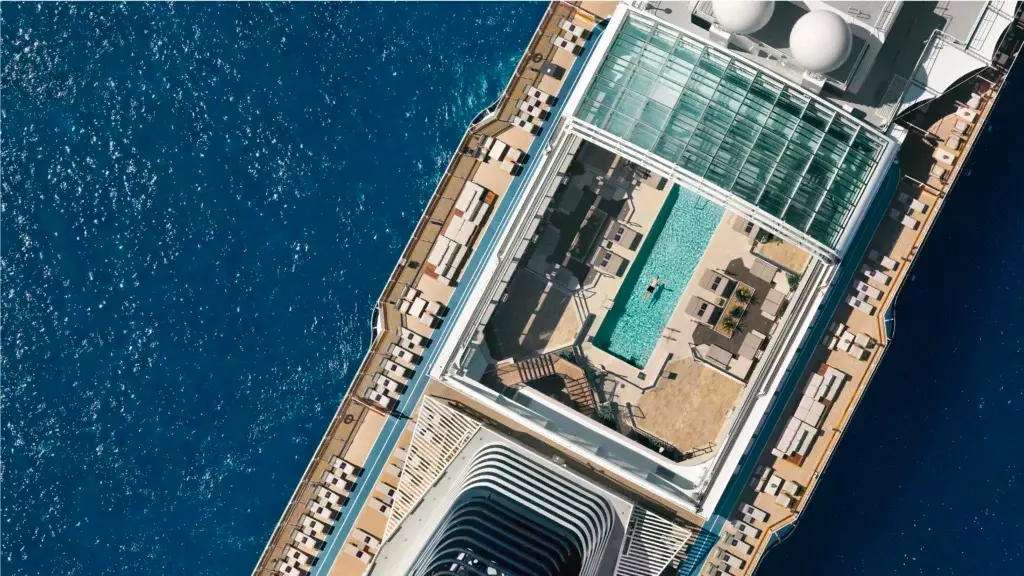 Vista aérea cenital de la piscina principal del barco con su icónica cubierta de cristal y áreas de solárium de diseño