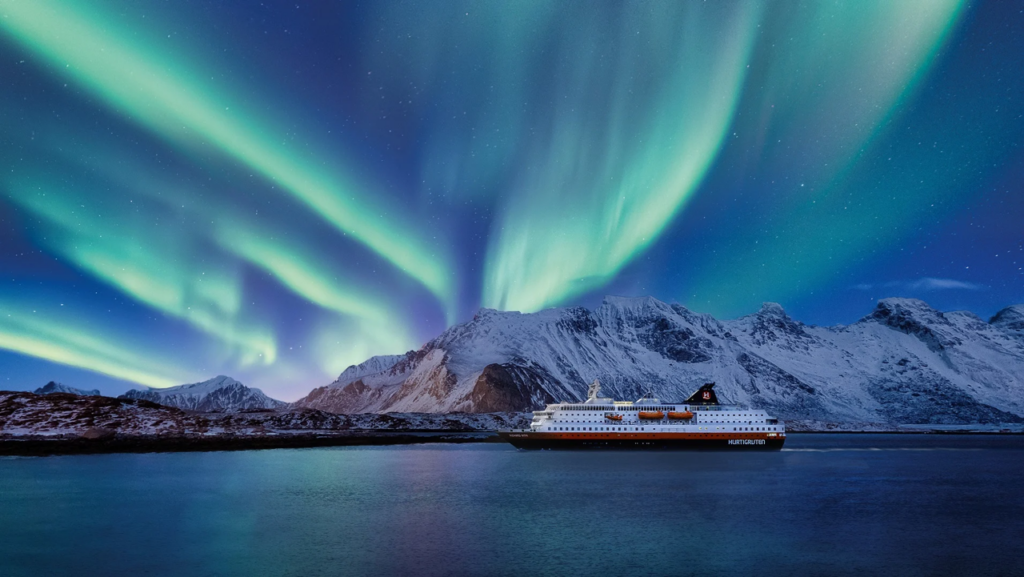 Barco de la naviera Hurtigruten navegando bajo una intensa aurora boreal en las costas de Noruega durante la temporada de invierno 2026