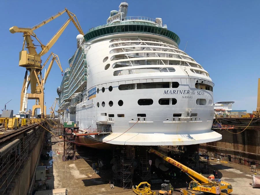 Primer plano trasero del Mariner of the Seas en dique seco para mantenimiento técnico con grúas amarillas.