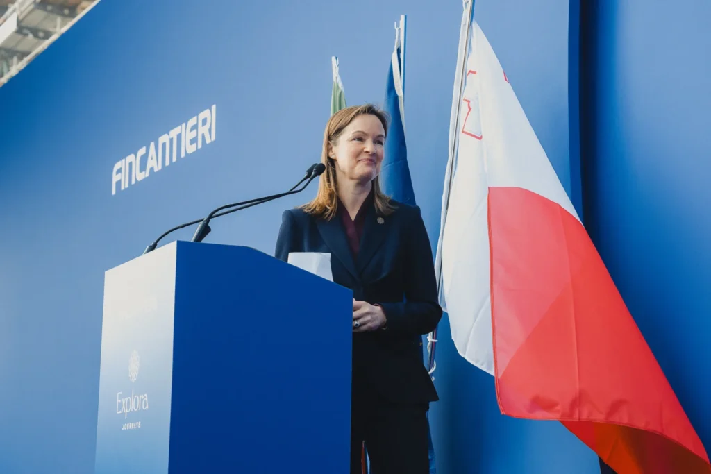 Anna Nash, Presidenta de Explora Journeys, interviniendo en el escenario principal frente a una gran pantalla con la imagen de un buque de la flota