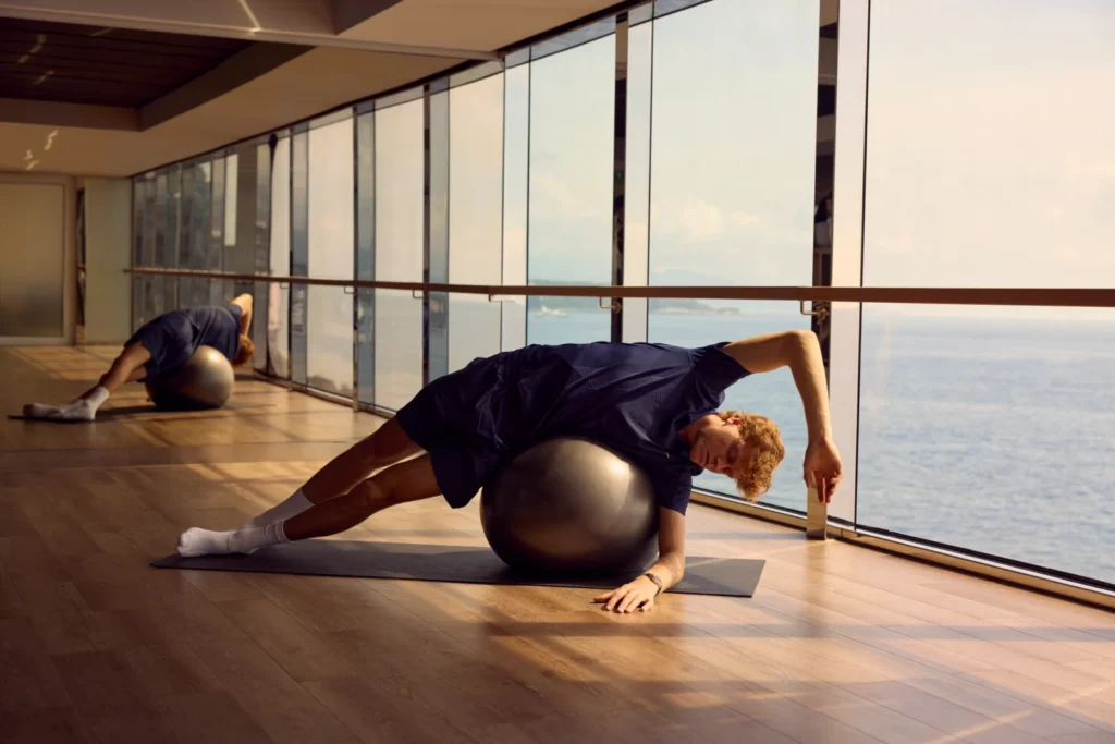 Jannik Sinner haciendo ejercicio con una pelota de yoga en un gimnasio de crucero con vistas panorámicas al océano
