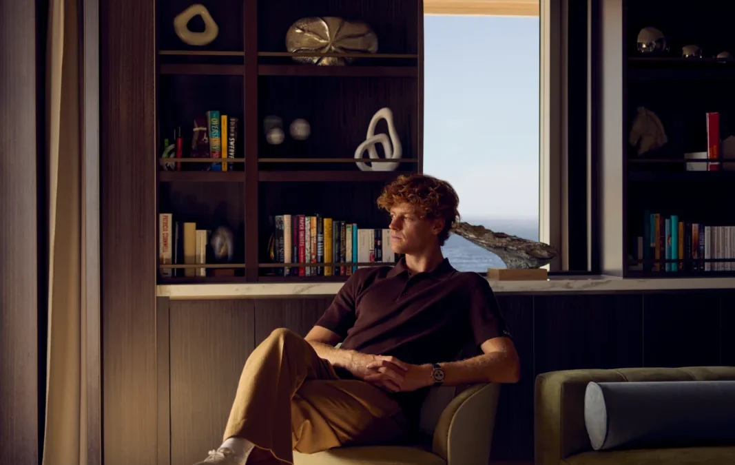 Jannik Sinner se relaja en un sillón de diseño en una lujosa cabina suite de crucero con ventanales al mar