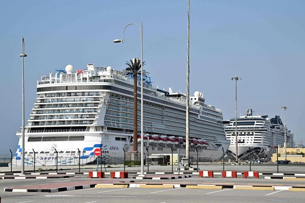 Crucero blanco de lujo Aroyia atracado en un puerto marítimo con bolardos y cercas en primer plano bajo un cielo azul claro