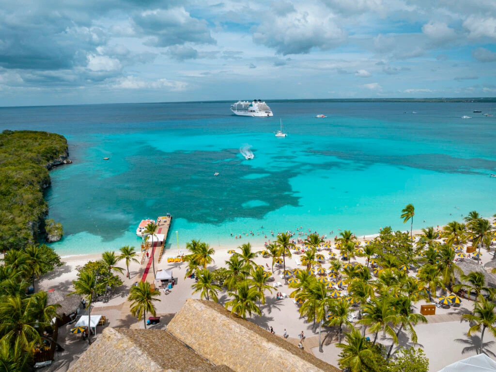 Vista aérea de la costa de Isla Catalina en La Romana con un barco de crucero fondeado y playas de arena blanca rodeadas de vegetación tropical.