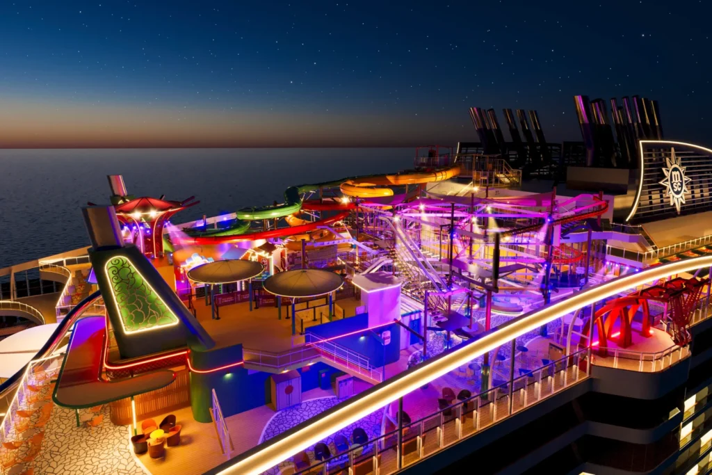 Vista nocturna de las cubiertas superiores del crucero MSC World Asia con toboganes iluminados.