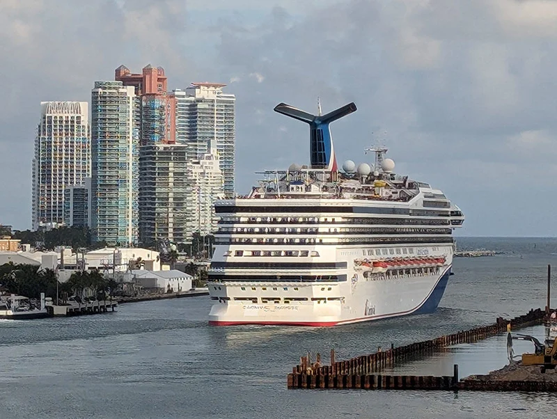 Un crucero Carnival navegando por el canal de salida del puerto de Miami frente a los rascacielos de la ciudad.