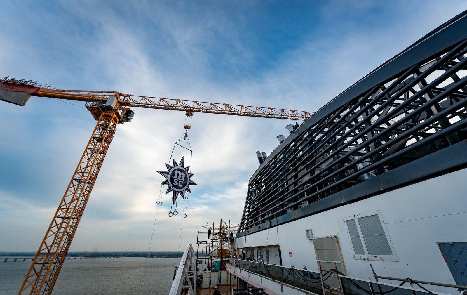 Una grúa de construcción eleva el logo de MSC con forma de brújula hacia la estructura superior de un crucero.