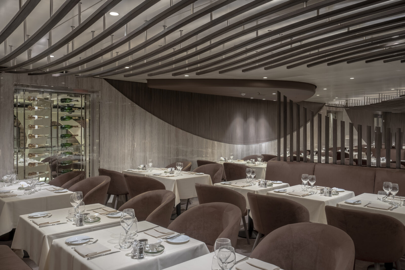 Comedor de restaurante a bordo de un crucero con mesas preparadas, manteles blancos y sillones color marrón.