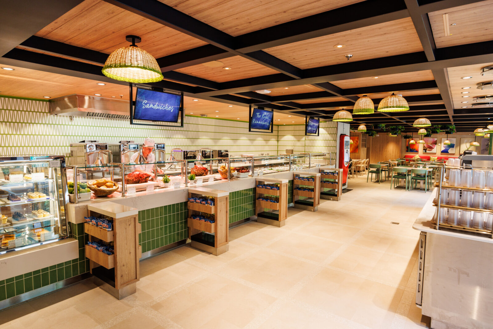 Área de buffet moderna con mostrador de comida, letreros digitales y zona de mesas al fondo