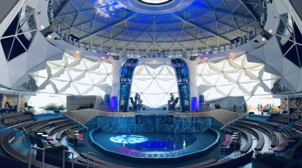 Interior del Aquadome con piscina, escenario y estructura de domo geodésico en el barco Icon of the Seas.