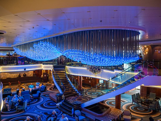 Vista interior del atrio de un crucero con una gran instalación de luces azules colgantes sobre una escalera central.