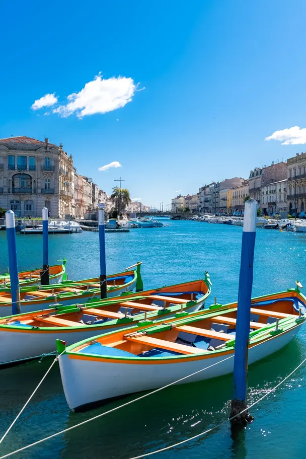Barcas coloridas amarradas en un canal mediterráneo bajo un cielo azul brillante y edificios históricos