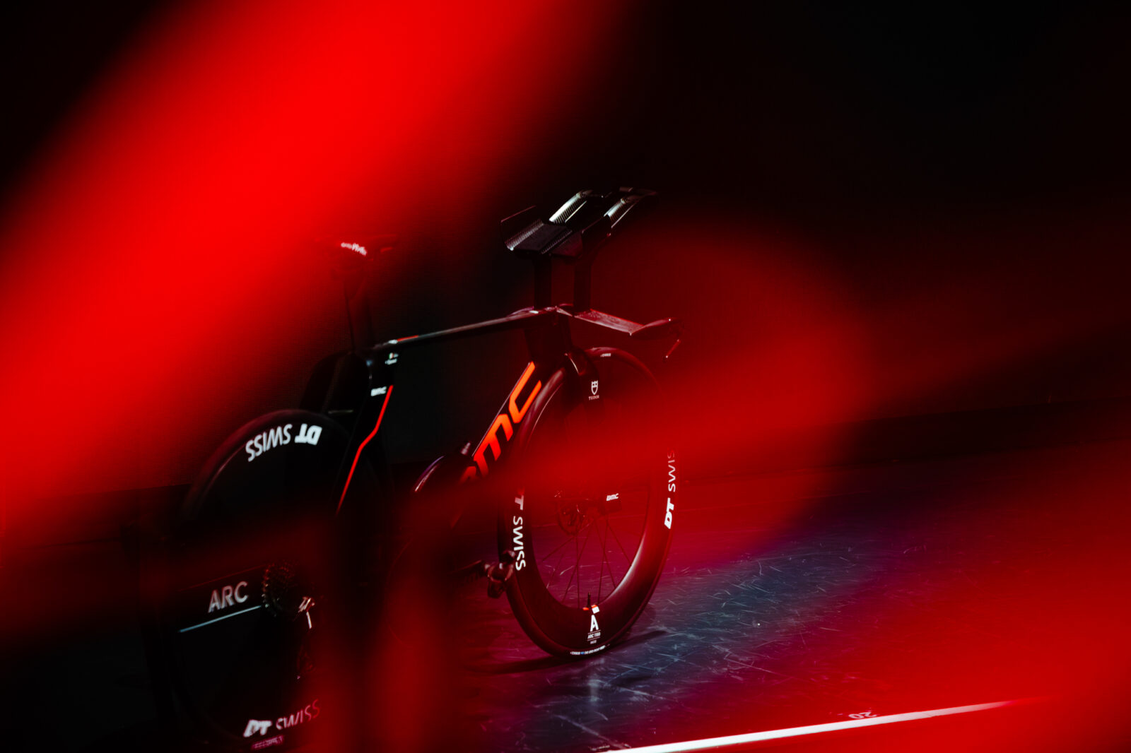 Bicicleta de contrarreloj BMC con ruedas DT Swiss sobre un escenario iluminado con luces rojas intensas.