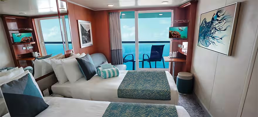 Interior de un camarote de crucero con dos camas individuales, decoración moderna y un balcón privado con vistas al mar.