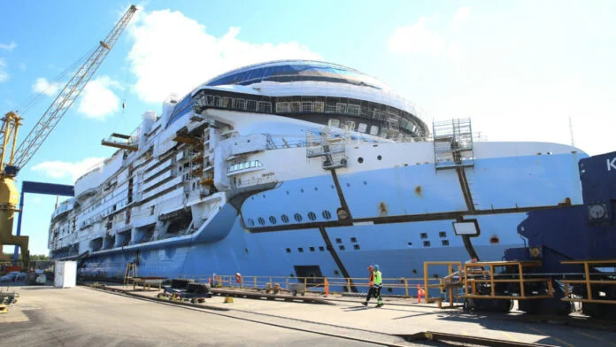 Vista lateral del casco de un gran crucero en construcción en un astillero de Finlandia con grúas visibles.