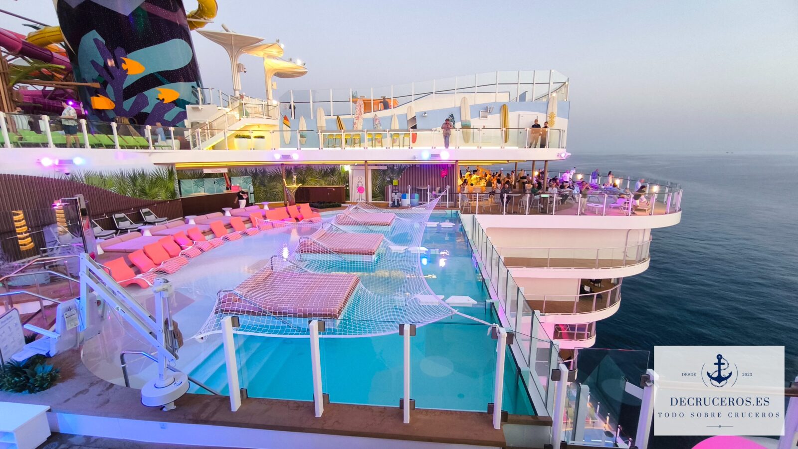 Piscina con tumbonas sumergidas y redes en la cubierta exterior de un crucero Clase Icon al atardecer.