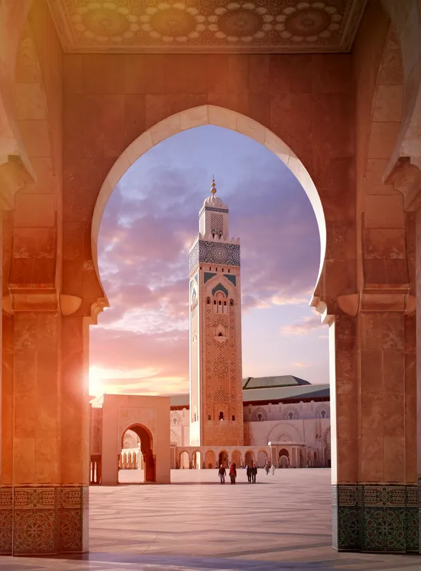 Vista a través de un arco de piedra hacia el minarete de la Mezquita Hassan II al atardecer en Casablanca.