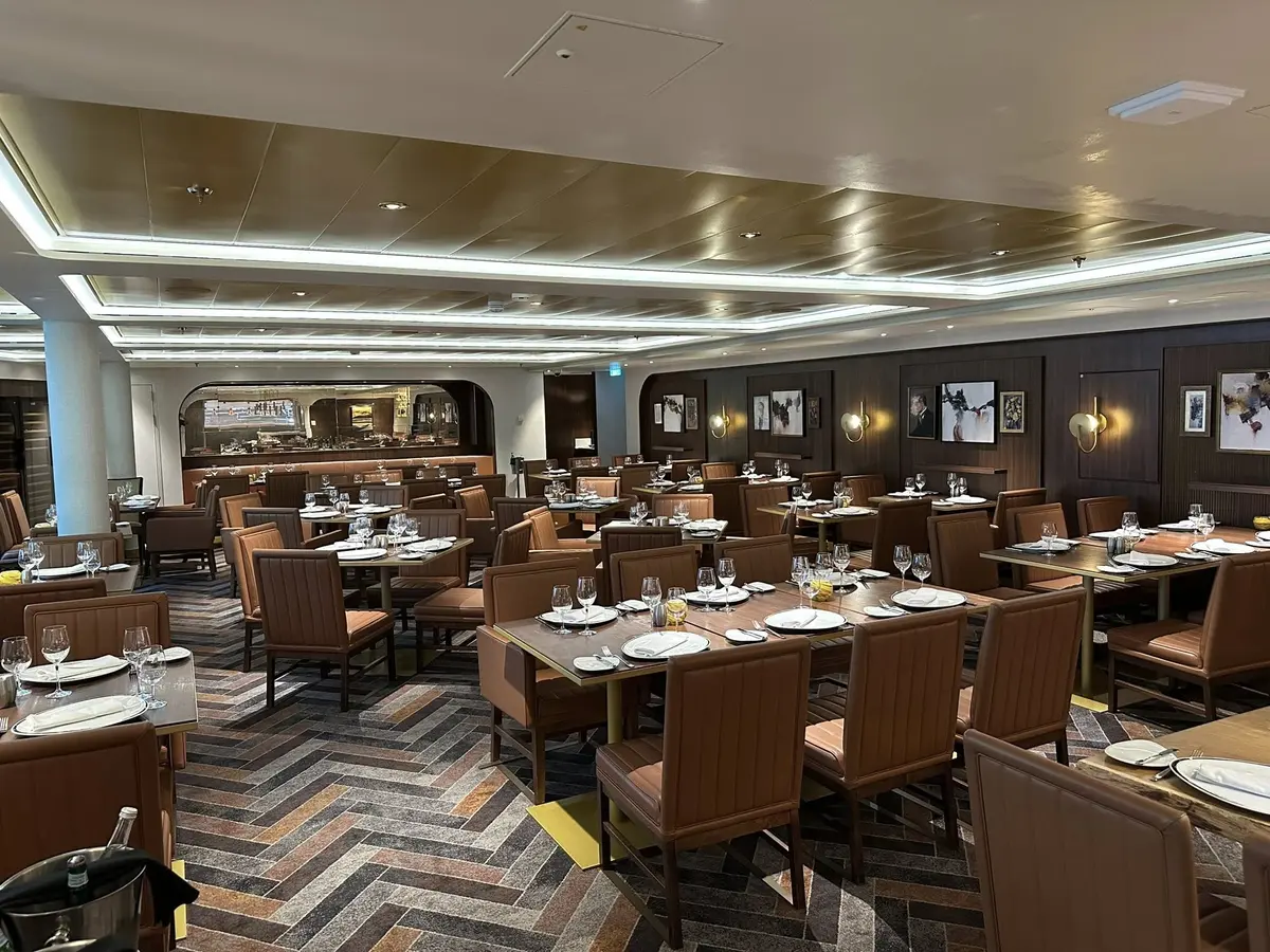Interior elegante del restaurante Chops Grille con mesas dispuestas y sillas de cuero marrón en el crucero Icon of the Seas.
