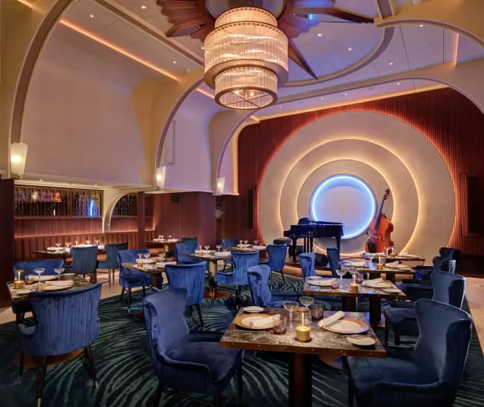 Interior del elegante Empire Supper Club en el barco Icon of the Seas con mesas dispuestas frente a un escenario.