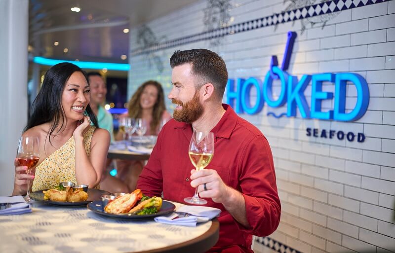Pareja cenando y brindando con vino en el restaurante Hooked Seafood a bordo del crucero Icon of the Seas.