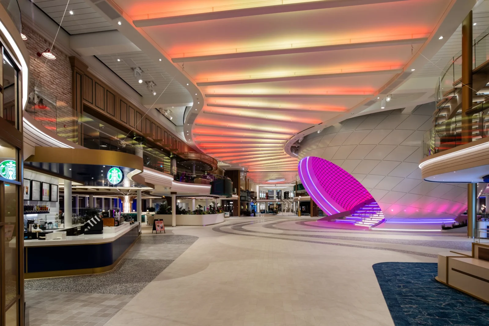 Interior del Royal Promenade en un crucero clase Icon de Royal Caribbean con iluminación LED y un Starbucks.